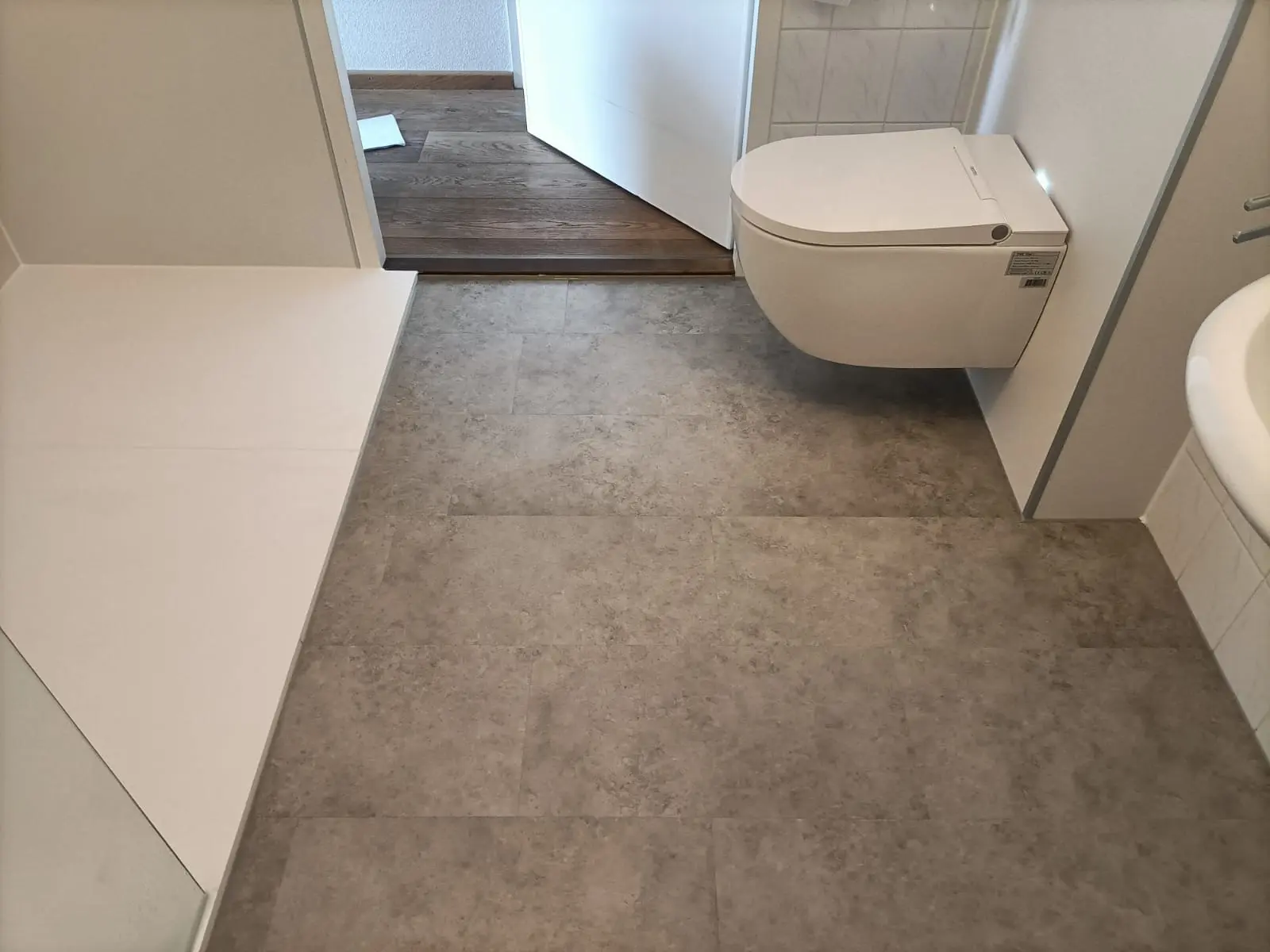Wandhangend douchetoilet naast witte douchevloer op grijze steenlook vloer