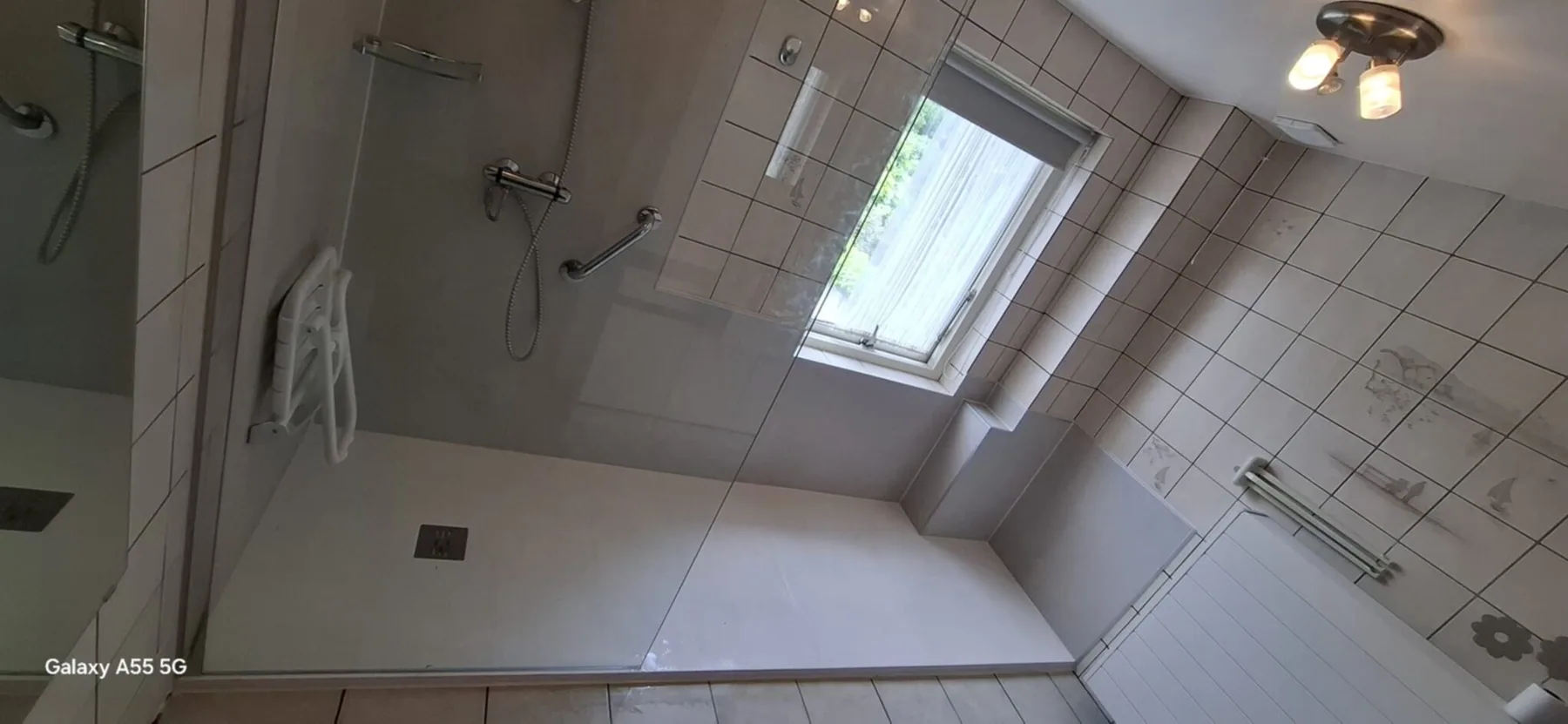 Brede inloopdouche na renovatie Brede inloopdouche bij het raam met douchezitje, steunbeugel en glazen wand