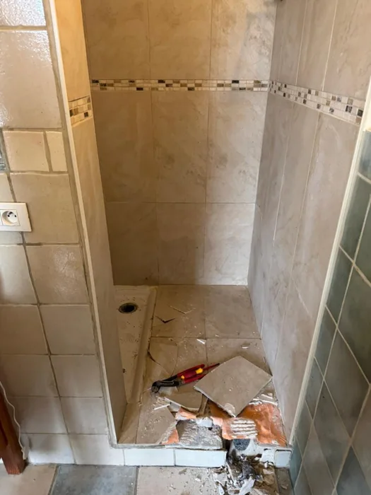 Douche tijdens sloopwerk: vloertegels eruit, afvoer zichtbaar, beige wandtegels met mozaïekrand