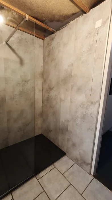 Douchehoek met gevlekte steenlook wandpanelen Douchehoek met gevlekte steenlook wandpanelen, glazen wand en zwarte douchebak