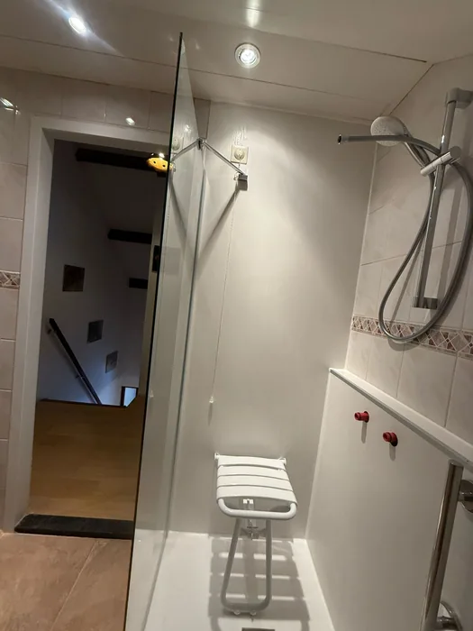 Douche met zitje Inloopdouche met witte panelen, opklapbaar douchezitje en glazen deur naar de overloop