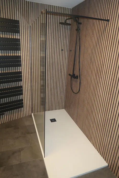 Inloopdouche met witte douchebak Inloopdouche met witte douchebak, glazen wand en zwarte regendouche tegen houten lamellenpanelen