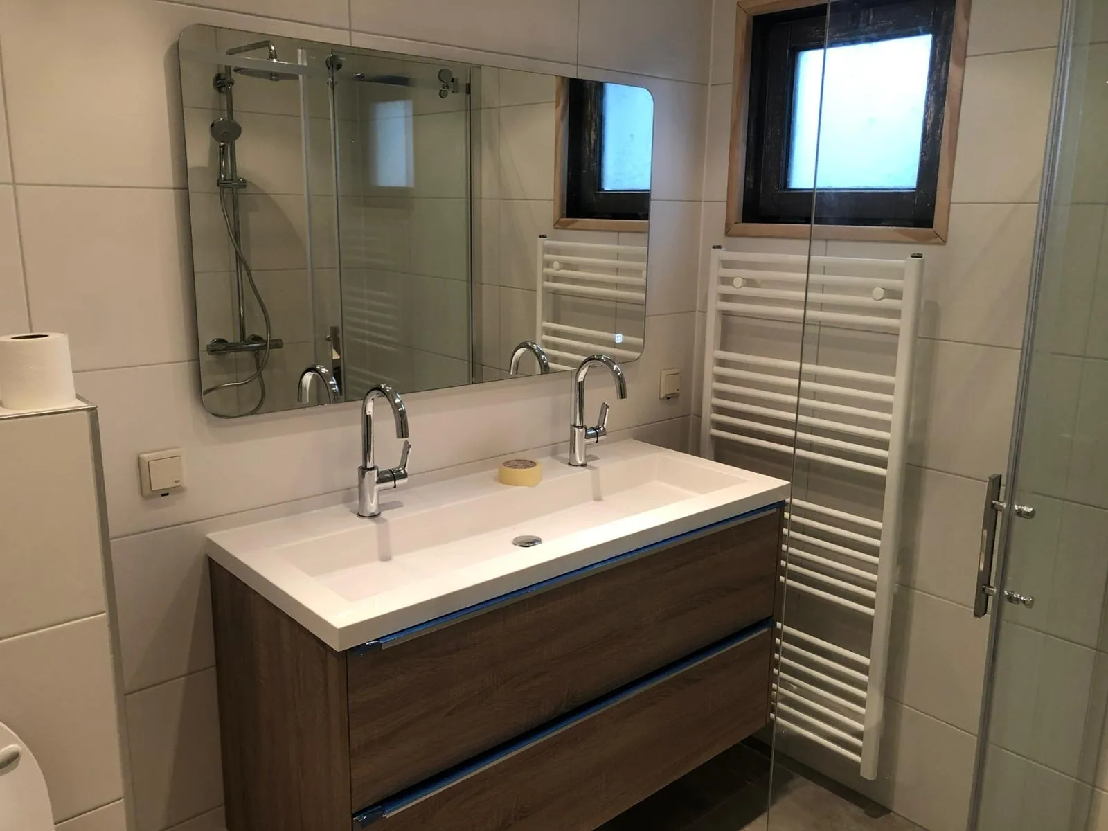 Vernieuwde badkamer met dubbel badmeubel Nieuwe badkamer met dubbele wastafel op houten meubel, spiegel, handdoekradiator en glazen douchewand